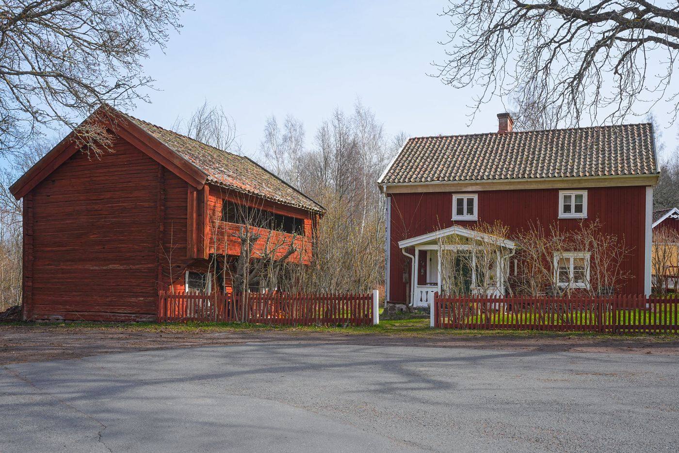 Gårdsmiljö med rött bostadshus och äldre timrad ekonomibyggnad