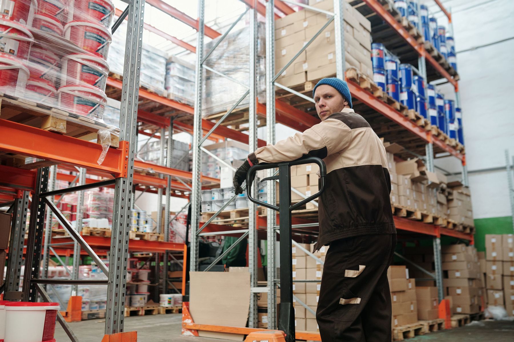 Lagerarbetare med pallyftare mellan fyllda pallställ